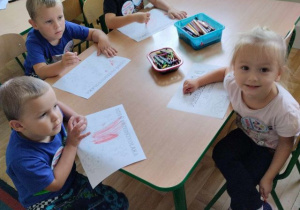 Dzieci siedzą przy stoliku i kolorują obrazki.