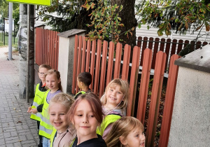 Dzieci podczas spaceru, na chodniku w kamizelkach odblaskowych.