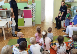 Panie policjantki w towarzystwie dzieci demonstrują zasady przechodzenia przez przejście dla pieszych z sygnalizatorem świetlnym - kolejne ujęcie.