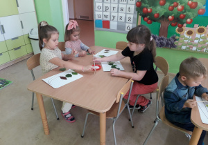 Przedszkolaki przy stolikach z zasuszonych liści tworzą jesienny obrazek.