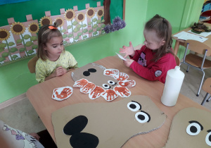 Dziewczynki naklejają odciśnięte "łapki" na sylwetę "jeża mamy" i "małego jeżyka".