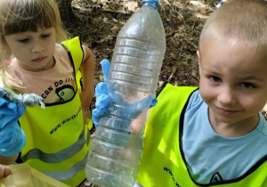 Dziewczynka i chłopiec wrzucają palstikową butelkę do żółtego worka.