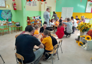 Dzieci wspólnie z rodzicami wycinają dyniowe minki.