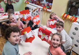 Dzieci siedzą przy stoliku i prezentują godło.