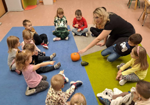 Dzieci siedzą w kole. Nauczyciel prezentuje dynię