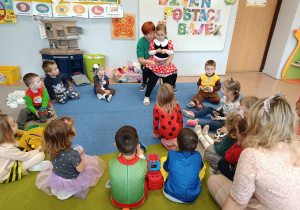 Mama dziewczynki czyta książkę grupie dzieci 3-4 letnich siedzących na dywanie