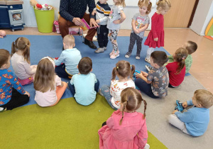 Tata chłopca czyta książkę grupie dzieci 3-4 letnich siedzących na dywanie