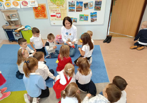Mama chłopca czyta książkę grupie dzieci 3-4 letnich siedzących na dywanie