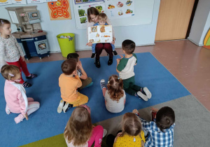 Mama chłopca czyta książkę grupie dzieci 3-4 letnich siedzących na dywanie