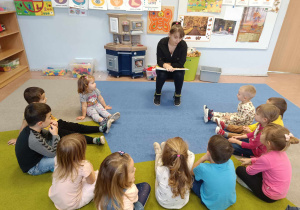 Mama chłopca czyta książkę grupie dzieci 3-4 letnich siedzących na dywanie