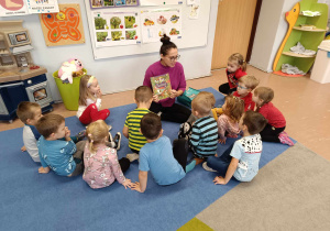 Mama dziewczynki czyta książkę grupie dzieci 3-4 letnich siedzących na dywanie