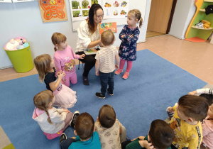 Mama dziewczynki czyta książkę grupie dzieci 3-4 letnich siedzących na dywanie