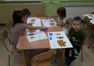 Dzieci przy stolikach wykonują pracę plastyczną z jesiennych liści.