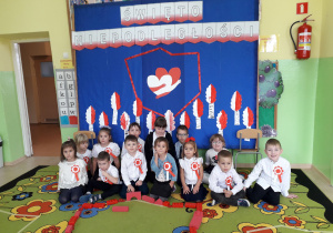 Przedszkolaki pozują na tle patriotycznej dekoracji.