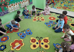 Dzieci na dywanie konstruują figury geometryczne z drewnianych patyczków.
