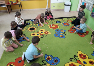 Dzieci na dywanie konstruują figury geometryczne z drewnianych patyczków.