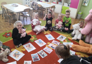 Przedszkolaki siedzą w kole. Ogladają obrazki przedstwiające bajkowe misie i słuchają historii o misiu.