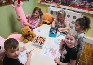 Starszaki siedzą przy stoliku i kolorują obrazki misia.