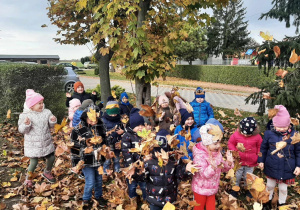 Dzieci z grupy 3,4,5 latków na powietrzu podczas zabawy ruchowej z liśćmi.
