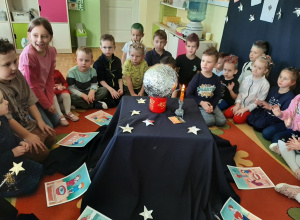 Przedszkolaki siedzą na dywanie wokół magicznego stolika, na którym stoi srebrna kula, świeci elektryczna świeczka.