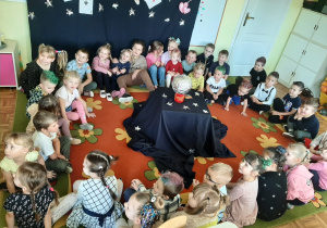 Dzieci siedzą w kręgu. W środku magiczny stolik ze srebrną kulą.