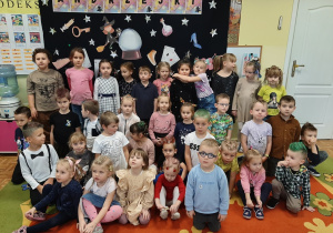 Przedszkolaki pozują do zdjęcia na tle andrzejkowej dekoracji, prezentują swoje fryzury.