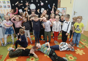 Dzieci z grupy 5,6 latków pozują do fotografii na tle andrzejkowej dekoracji. Robią śmieszne miny, prezentują fryzury.