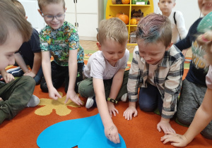 Kilku chłopców na dywanie, jeden z nich przebija papierowe serce pinezką, kolejne ujęcie.