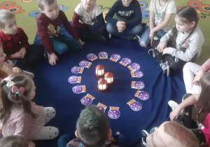 Dzieci siedzą w kole, na środku karty do wróżb i lampiony