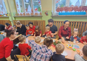 Dzieci i rodzice siedzą przy stole i dekorują pierniki