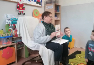 Pani bibliotekarka siedzi na fotelu i czyta dzieciom bajkę
