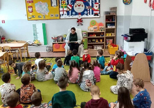 Pani bibliotekarka siedzi na fotelu i czyta dzieciom bajkę