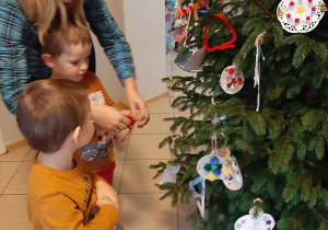 Rodzic z dziećmi wiesza na choince wykonane ozdoby.