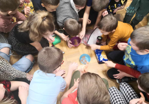 Dzieci siedzą w kole, rozpoznają produkty potrzebne do przygotowania ciasta piernikowego.