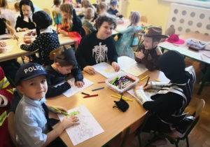 Chłopcy siedzą przy stoliku i kolorują obrazki.