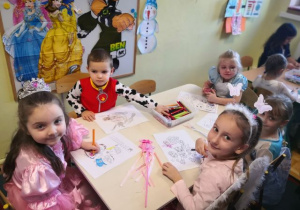 Dzieci siedzą przy stoliku i kolorują obrazki.