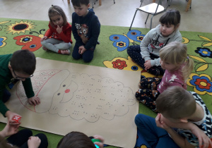 Dzieci na dywanie w sali bawią się z kostką i sylwetą Mikołaja.