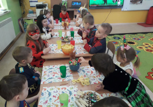 Poczęstunek karnawałowy. Dzieci przy stolikach częstują się karnawałowymi przekąskami.