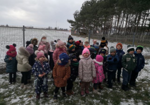 Przedszkolaki stoją koło karmnika.