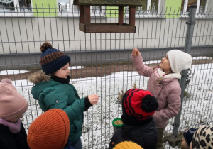 Dzieci wsypują ziarenka do karmnika.