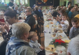 Babcie i dziadkowie siedzą przy stołach na holu przedszkolnym