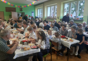 Babcie i dziadkowie siedzą przy stołach na holu przedszkolnym