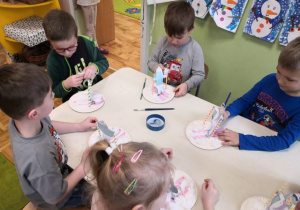 Dzieci siedzą przy stoliku i wykonują pracę plastyczno-techniczną.