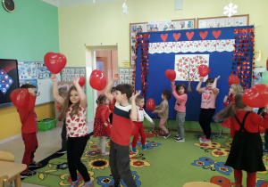 Zabawy taneczne dzieci z balonami na tle walentynkowej dekoracji.