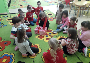 Dziewczynka w gronie przedszkolaków otwiera walentynkową skrzynkę.
