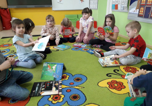 Dzieci na dywanie prezentują swoje ulubione książeczki z bajkami.