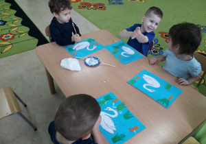 Dzieci przy stolikach wykonują pracę plastyczną "Brzydkie kaczątko".