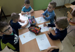 Dzieci przy stolikach kolorują głowę smoka.