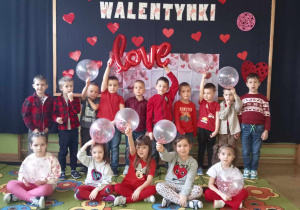 Dzieci w grupie z balonami. W tle dekoracja walentynkowa.