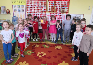 Przedszkolaki pozują do zdjęcia, na dywanie ułożone jest przez dzieci duże serce z serduszek.